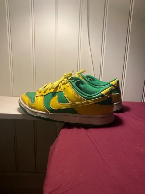 Nike Dunk Low gul/grön skate sneakers - Nike Dunk Low sneakers i en fet färgkombo med gröna och gula paneler, gula snören och vit mellansula. Skorna har rund tå, platt sula och är tillverkade i skinn. Perfekt för dig som vill sticka ut med klassiska dunks i streetwear-stil. Ganska använda men har ändå en del kvar att ge, inga galna stora skador eller defekter, bara hårt använda. Köpte för 1400 kr nypris och säljer rätt billigt nu.