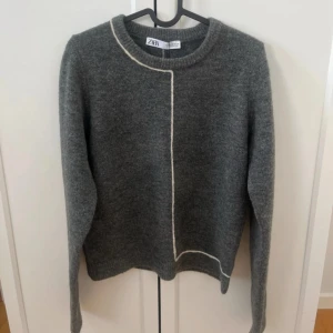 Grå stickad tröja från Zara - Mysig grå stickad tröja från Zara med vit kontrastsöm som går längs framsidan och bak. Rund halsringning och långa armar. Knappt andvänd.  storlek M men sitter som S då den har lite ”slim fit”. Priset går att diskutera.💗💗