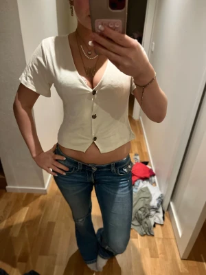 Vit croppad blus från Lager 157 - Säljer en vit croppad blus från Lager 157 i storlek S. Toppen har korta ärmar, v-ringning och tre knappar framtill. Den är figurnära och har en snygg, enkel design som är lätt att matcha med jeans eller kjol. Perfekt för dig som gillar stilrena och trendiga plagg.