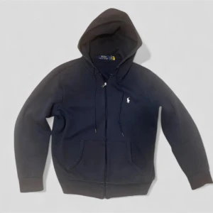 Mörkblå Ralph Lauren zip hoodie  -   *   Märke: Polo Ralph Lauren *   Skick: Använd, som ny *   Användning: Använd ett fåtal gånger *   Design: Klassisk design med huva och fickor *   Färg: Svart *   Defekter: Inga *   Nypris: 1200 kr *   Pris: Bud *   Finns i Göteborg  En snygg och bekväm hoodie för alla tillfällen! PM vid intresse.