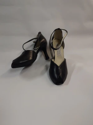 Svarta Dansskor med klack och rem - Snygga svarta pumps från Werner kern med elegant klack och smal rem runt ankeln. Skorna har en spetsig tå och är tillverkade i skinn, vilket ger en stilren och klassisk look. Perfekta för dig som gillar tidlös design med en modern twist.