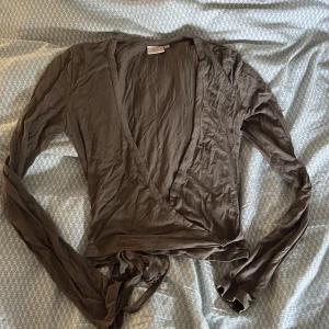 Brun omlottopp Nelly - Säljer en brun omlottopp från Nelly i storlek S. Toppen har långa ärmar, djup v-ringning och knyt i midjan för en snygg siluett. Materialet är mjukt och lätt, perfekt för att skapa en chill och trendig look. Köpt second hand men i fint skick, dock lite skrynklig men går att fixa
