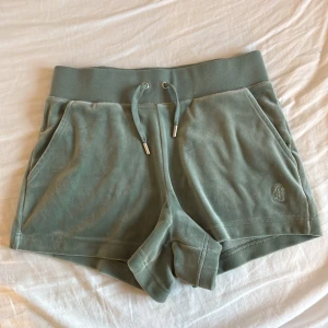 Gröna velourshorts Juicy Couture XS (ny utan prislapp) - Mysiga ljusgröna shorts från Juicy Couture i velour med snörning i midjan och broderad JC-logga framtill. Shortsen har två fickor fram och två bakfickor med knappar. Perfekta för chill dagar eller när du vill ha en retro vibe.
