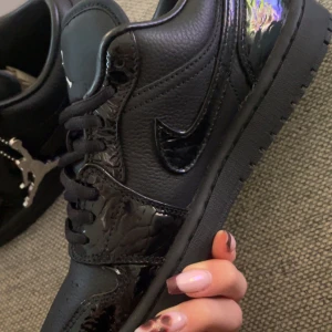 Jordan 1 low svart - Svarta nike jordan 1 low men glansiga detaljer. Tidigare kostat mer än hälften, skriv priv för gamla pris/+skärmdump
