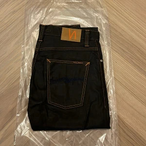 Helt nya Nudie jeans co - grim Tim - W31 L32 - Helt nya och oanvända Nudie Jeans Co Grim Tim i den exklusiva färgen Dry Black Coated – fortfarande i originalförpackning (se bilder).  Detta är en av Nudies mest populära modeller, med en tidlös passform och den välkända premiumkvaliteten som gör Nudie till ett av Sveriges mest uppskattade jeansmärken.  Nypris: 1600  Detaljer: • Modell: Grim Tim • Storlek: W31 / L32 • Färg: Dry Black Coated (svart med lätt glans och vaxad look) • Passform: Regular slim fit – normal midja, rakare ben