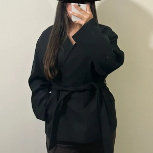 Svart Zina kappa med bälte från Bik Bok (strl S) - Svart Zina kappa från Bik Bok med bälte i midjan och v-ringad hals. Strl S, slutsåld på hemsidan!                                                            Ny med prislapp, original priset 699kr.             Skriv om flera bilder önskas 🥰