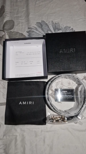 Svart skärp från Amiri med guldspänne - Snyggt svart bälte från Amiri i äkta skinn med ett unikt guld- och svartfärgat metallspänne i form av Amiris logga. Bältet är stilrent och passar perfekt till jeans eller kostymbyxor. Levereras med originalbox och dustbag.