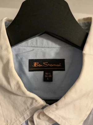 Blå skjorta med vit krage Ben Sherman - Snygg ljusblå skjorta från Ben Sherman med kontrasterande vit krage och vita knappar. Klassisk design med lång ärm och rak passform, perfekt för dig som gillar stilrena detaljer. Skjortan är gjord i mjuk bomull som känns skön mot huden.