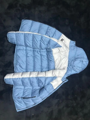 Blå och vit pufferjacka McKenzie L kan diskutera om priset - Säljer en blå och vit pufferjacka från McKenzie i storlek L. Jackan har huva, dragkedja och quiltad design. Materialet är polyester med återvunnen vaddering. Perfekt för kalla dagar med sin vind- och vattenavvisande funktion.