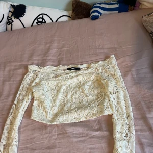 Vit spetsig croppad topp från Bik Bok - Säljer en vit croppad topp från Bik Bok med långa ärmar och offshoulder-modell. Toppen är helt i spets med blommigt mönster och har en romantisk vibe. Perfekt för dig som vill sticka ut med en feminin och trendig look.
