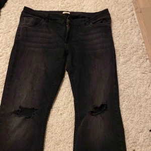 Svarta jeans med slitna knän - Snygga svarta jeans från Nelly med slitningar på båda knäna och klassisk femficksmodell. Bakfickan har en cool broderad detalj i form av ett zigzag-mönster. Jeansen är bootcut och är perfekta för en avslappnad streetstil.