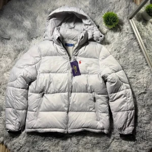 Ljusgrå pufferjacka från Polo Ralph Lauren - Snygg ljusgrå pufferjacka från Polo Ralph Lauren med huva och klassisk röd logobrodyr på bröstet. Jackan har dragkedja framtill, två sidofickor med dragkedja och quiltad design. Perfekt för kalla dagar och riktigt clean look.