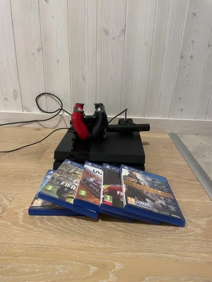 PlayStation 4 packet med ny kylpasta - Komplett PlayStation 4 med två DualShock 4-kontroller (röd och svart), PlayStation Camera, laddstation och fem spel. Konsolen och tillbehören är i gott skick med endast mindre bruksspår. Perfekt för familj eller gamingkvällar, hdmi följer också med om det behövs. Gjorde också rengöring på den precis inuti.