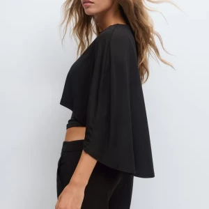 Svart croppad blus med vida ärmar - Säljer en svart croppad blus med vida, fladdriga ärmar och rund halsringning. Toppen har en snygg, lös passform upptill och sitter tightare vid midjan. Perfekt för dig som gillar en stilren och trendig look.