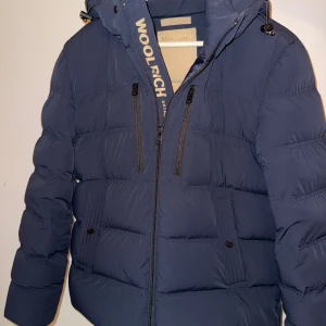Mörkblå pufferjacka från Woolrich - Woolrich down jacket i storlek M. Jackan är använd en gång och säljer eftersom jag inte tyckte om den marinblåa färgen och vill införskaffa en svart.  Kvitto finns. Skicka ett pm för mer info! Nypris 9100kr. 