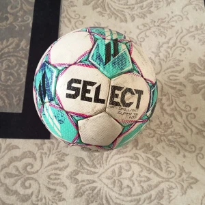 Select boll - Säljer en Select Brillant Super TB fotboll i storlek 5 med FIFA Quality Pro-märkning. Bollen har ett coolt mönster i vitt, turkos, lila och rosa med svarta detaljer. Ytan är strukturerad för bättre grepp och precision. Perfekt för matcher och träning.