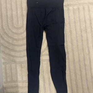 Svarta leggings från H&M Move - Snygga svarta leggings från H&M Move i storlek M. De har en hög midja och är tillverkade i ett stretchigt syntetmaterial som sitter tight och bekvämt. Perfekta för träning eller chill dagar. Stilren design utan synliga detaljer.