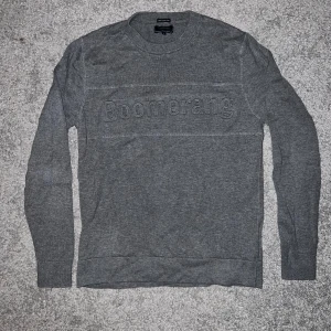 Grå tröja från Boomerang - Säljer en stilren grå tröja från Boomerang med broderad logga framtill. Tröjan har rund halsringning och långa ärmar, perfekt för lager-på-lager. Skön och enkel att matcha till jeans eller chinos.