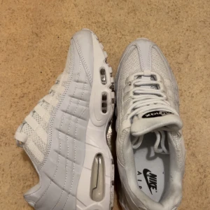 Nike Air Max vita sneakers - Fräscha vita Nike Air Max sneakers med synlig luftdämpning i sulan och klassisk snörning. Skorna har en sportig design med mesh och syntetpaneler för extra komfort och stil. Perfekta för dig som gillar streetwear och vill ha en clean look.