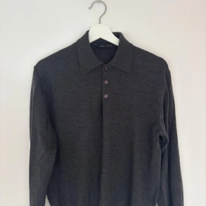 Mörkgrå stickad pikétröja - Mörkgrå stickad pikétröja från Fathers & Sons med klassisk krage och tre knappar framtill. Långärmad modell i mjukt material som passar perfekt till lager-på-lager. 