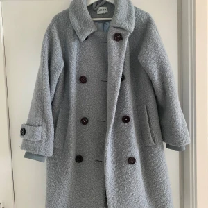 Ljusgrå teddyrock från Ganni - Säljer en ljusgrå teddyrock från Ganni med bred krage och stora bruna knappar framtill. Jackan har långärmade ärmar med knappdetalj vid mudden och två sidofickor. Materialet är mjukt och fluffigt, perfekt för kyliga dagar. Jackan är i storlek s men passar även M. 