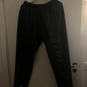 Svarta mjukisbyxor från Gasp strl M - Svarta mjukisbyxor från Gasp i storlek M med tryckt logga längs ena benet. Byxorna har elastisk midja med snörning och sidofickor. Perfekta för chill eller gym, riktigt sköna och stilrena.