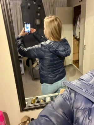 Mörkblå pufferjacka från Peak Performance - Säljer en mörkblå pufferjacka från Peak Performance med huva och dragkedja. Jackan är vadderad och har en clean look med diskret logga på bröstet och ärmen. Perfekt för kalla dagar och riktigt skön att bära. Långärmad och normal passform.