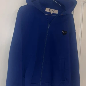 Blå hoodie från Comme des Garçons Play  - Blå hoodie från Comme des Garçons Play i storlek M. Tröjan har dragkedja, huva och det ikoniska svarta hjärta med ögon på bröstet samt ett stort hjärta med ögon på ryggen. Bra skick, använd några gånger. Pris kan diskuteras vid snabb affär!