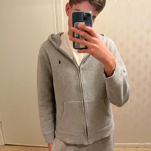 Zip hoodie Polo Ralph Lauren - Säljer en grå hoodie från Polo Ralph Lauren med dragkedja och huva. Tröjan har två fickor framtill, långärmad design och ett broderat Polo-logo på bröstet. Tillverkad i mjuk bomullsfleece som är skön att ha på sig. Jag skulle säga att den är runt storlek XS själv är jag storlek S och 182cm lång och sitter så på mig som på bilden
