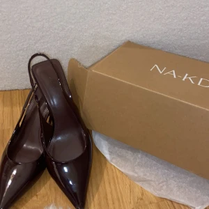 Brundgurdy spetsiga pumps NA-KD - Säljer dessa sprillans nya klackar från NA-KD. Färgen är ”brundgurdy” = en blandning av /mörklila/vinröda.  Klackarna är spetsiga med en snygg glans. Skorna har öppen häl med rem och låg klack. Tillverkade i syntetmaterial, jätte classy och går till allt. Köpte för 499, och säljer för 400. Då de är helt oanvända, och i orginal paketet. Tveka inte på att höra av dig 🩷