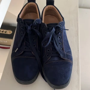 Loubs - Snygga mörkblå sneakers i mocka med klassisk snörning och rund tå. Skorna har en unik röd sula med mönstrad textur och beige innersida. Perfekta för dig som vill sticka ut med en cool detalj på fötterna.