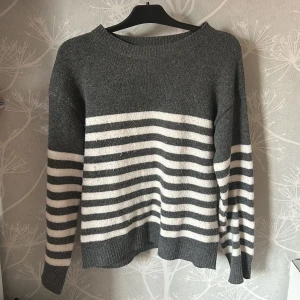 Randig grå och vit stickad tröja - Mysig stickad tröja i grått och vitt med breda horisontella ränder över kroppen och ärmarna, perfekt för kyligare dagar.