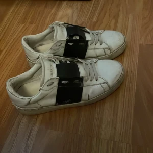 Valentino Garavani Open sneakers vit/svart - Säljer ett par Valentino Garavani Open sneakers i vitt skinn med bred svart läderdetalj över vristen och ikoniska nitar på sulan. Dom är äkta men dom är använda och slitna där av priset, dom är också lite smutsiga men det går säkert att få rent 