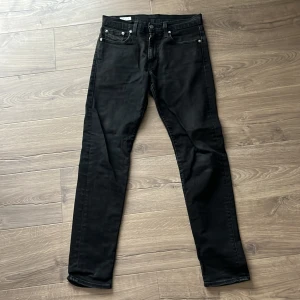 Levi's 512 svarta jeans W29 L32 - Svarta Levi's 512 jeans med slim fit och klassisk femficksdesign. Jeansen har en smal passform med något avsmalnande ben och är tillverkade i ett mjukt jeansmaterial. Snygga detaljer som silverfärgade nitar och Levi's ikoniska röda etikett på bakfickan.