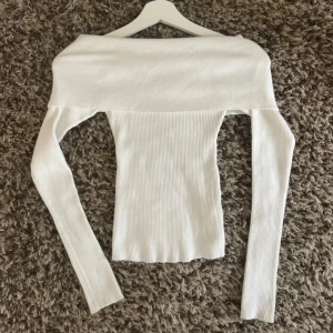 Vit ribbad offshoulder topp - Säljer en vit ribbad offshoulder topp med lång ärm. Toppen har en tight passform och är tillverkad i ett stretchigt material som sitter snyggt på kroppen. 