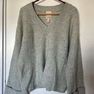 Ljusgrön stickad tröja från H&M - Superfin ljusgrön stickad tröja från H&M i lyxig alpacka- och ullblandning. Oversized passform med v-ringning, ribbade muddar och långa ärmar som är uppvikta i designen. Upplevs något ”grov” mot huden i och med ullen, men är väldigt varm och fin kvalité! Använd ca 3 gånger. Rymlig i passformen, passar lätt upp till L. Orginalpris 700 kr. 