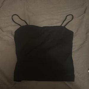 Svart linnetopp från Gina Tricot XS - Säljer en svart, enkel och stilren linnetopp från Gina Tricot i storlek XS. Toppen har tunna axelband och är tillverkad i mjuk bomull från deras hållbara kollektion. Perfekt att matcha med jeans eller kjol för en clean look.