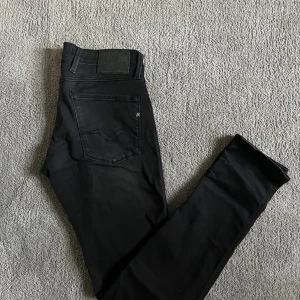 Svarta Replay jeans Anbass herr - Svarta jeans från Replay, modell Anbass. Klassisk femficksdesign med smal passform och diskreta detaljer. Jeansen är tillverkade i stretchig bomullsblandning för extra komfort och har en stilren look som passar till det mesta. Storlek 31/34