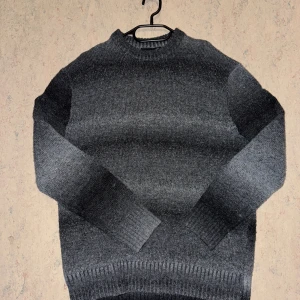 Mörkgrå stickad tröja med ombre - Snygg stickad tröja i mörkgrått med ombre-effekt. Tröjan har rund halsringning, långa ärmar och breda ribbade muddar vid ärmslut och nederkant. Perfekt för kyliga dagar och enkel att matcha med jeans eller kjol.