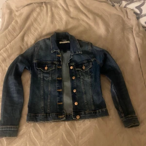 Klassisk jeansjacka från Weekday S - Snygg mörkblå jeansjacka från Weekday i klassisk modell med knappar i guldton, två bröstfickor med lock och långa ärmar. Jackan har en figurnära passform och är tillverkad i slitstarkt denim. Perfekt för dig som gillar en tidlös streetstil.