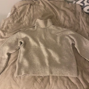 Beige polotröja från H&M - Mysig beige polotröja från H&M med ribbade muddar och hög krage. Tröjan är stickad och har en avslappnad passform med långa ärmar. Perfekt för kyliga dagar och enkel att matcha med jeans eller kjol.