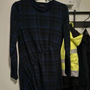 Mörkblå rutig långärmad klänning strl: L - Snygg långärmad klänning i mörkblått och svart med rutigt mönster och diskret rynkdetalj i midjan. Klänningen har rund halsringning och är i mjukt, lätt material som faller fint. Perfekt för dig som gillar en stilren men ändå intressant look.