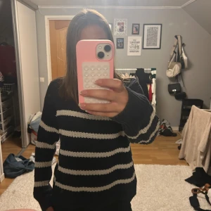 Randig stickad tröja i marinblått och vitt - Säljer en stickad tröja med breda marinblå och vita ränder. Tröjan har en klassisk rund halsringning, långa ärmar och ribbade muddar.