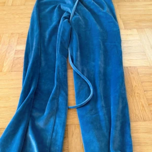 Blå sammetsmjukisbyxor från b.young - Blå mjukisbyxor i sammetsliknande material från b.young. Byxorna har dragsko i midjan och en loose passform, perfekta för en chill och avslappnad look. Materialet är mjukt och glansigt, vilket ger en lyxig känsla💗