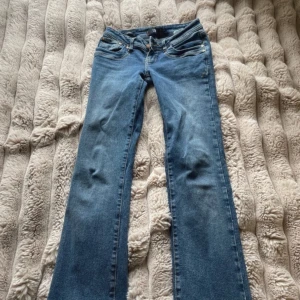 Blå bootcut jeans från LTB - Snygga blå jeans från LTB med klassisk bootcut-modell. Jeansen har fem fickor, guldfärgade nitar och kontrastsömmar. Materialet är jeans i bomullsmix och passformen är normal med medelhög midja. Perfekta för en avslappnad och trendig look.