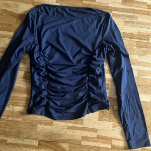 Mörkblå långärmad topp med rynk - Säljer en mörkblå långärmad topp med snygga rynkade detaljer längs sidorna och på ryggen. Toppen har en figurnära passform och är tillverkad i ett mjukt bomullsliknande material. Perfekt för dig som gillar stilrena plagg med en twist.