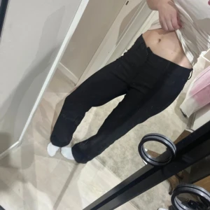 Svarta raka kostymbyxor - Säljer ett par svarta kostymbyxor med raka ben och låg midja. Byxorna har klassisk stängning med hyska och dragkedja samt fickor bak. Perfekta för en clean och stilren look. Annars i gott skick, förutom att ena spännet har lossnat, men byxorna sitter kvar med knappen.