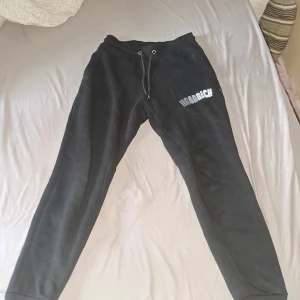 Svarta mjukisbyxor från Hoodrich XS - Svarta mjukisbyxor från Hoodrich i storlek XS. Byxorna har snörning i midjan och Hoodrich-logga tryckt på ena benet. Sköna och stilrena med klassisk passform, perfekta för chill eller streetwear. Tillverkade i mjukt material för extra komfort.