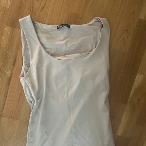 Beige ärmlös topp från Zara - Snygg beige ärmlös topp från Zara med rundad halsringning. Enkel och stilren design som passar perfekt till jeans eller kjol. Mjuk och lätt i materialet, vilket gör den skön att bära under varma dagar. Passar både XS och S.