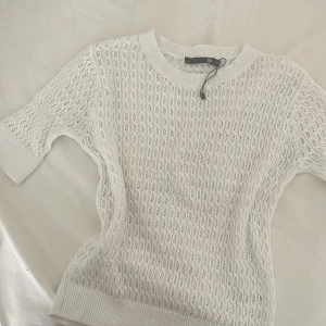 Vit stickad topp från 157, XS - Vit stickad topp från 157 i storlek XS. Tröjan har ett snyggt hålmönster, ribbade muddar och rund halsringning. Ärmarna är korta och materialet känns luftigt och mjukt, ja säljer för den inte kommer till användning och den är aldrig använd ❤️